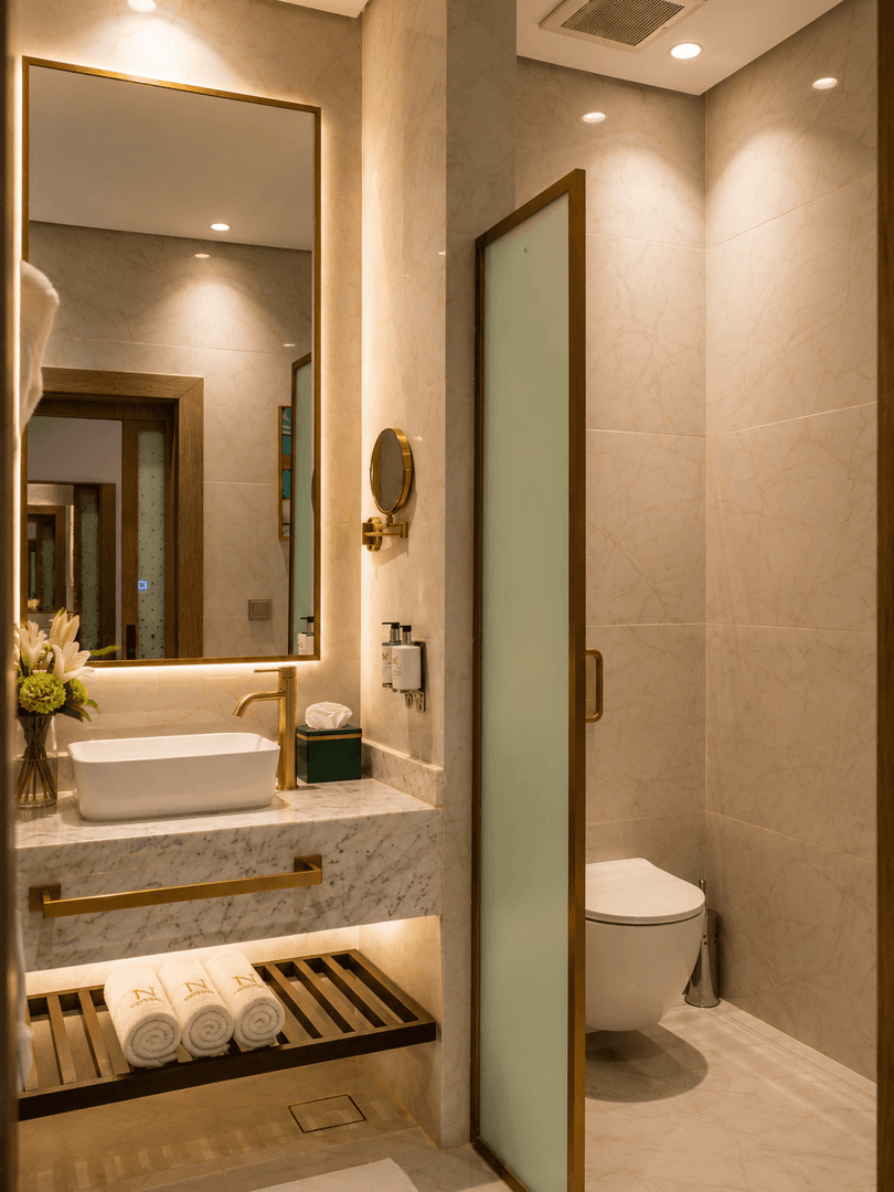 Deluxe Room bathroom vanity with gold faucet next to frosted glass partition wall at Naviti by Warwick Jeddah