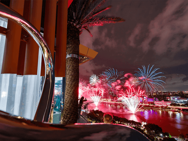 Nighttime fireworks over the river, viewed from a palm-lined balcony near Emporium Hotel South Bank