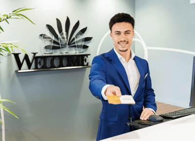 Smiling receptionist in a blue blazer handing over room keycards at the front desk beneath the welcome sign at Rodd Moncton