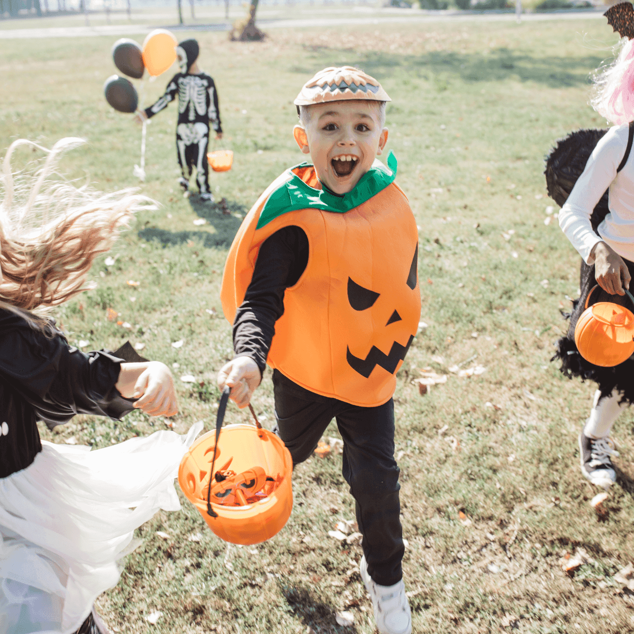 Children in Halloween costumes running with trick-or-treat buckets on a grassy field at Cider Hill Farm near The Exeter Inn