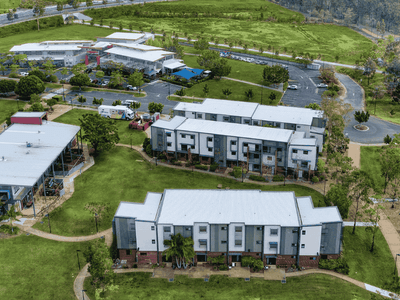 Aerial view of modern two-story residential buildings with white roofs surrounded by green lawns and trees in Springfield Central.