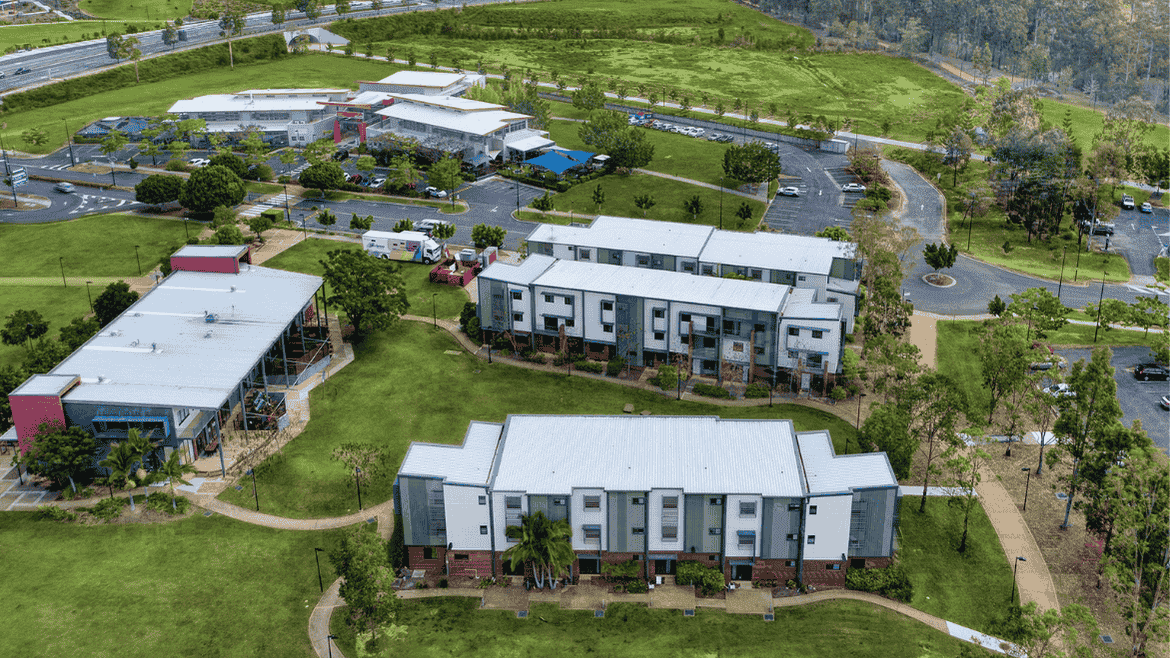 Aerial view of modern two-story residential buildings with white roofs surrounded by green lawns and trees in Springfield Central.