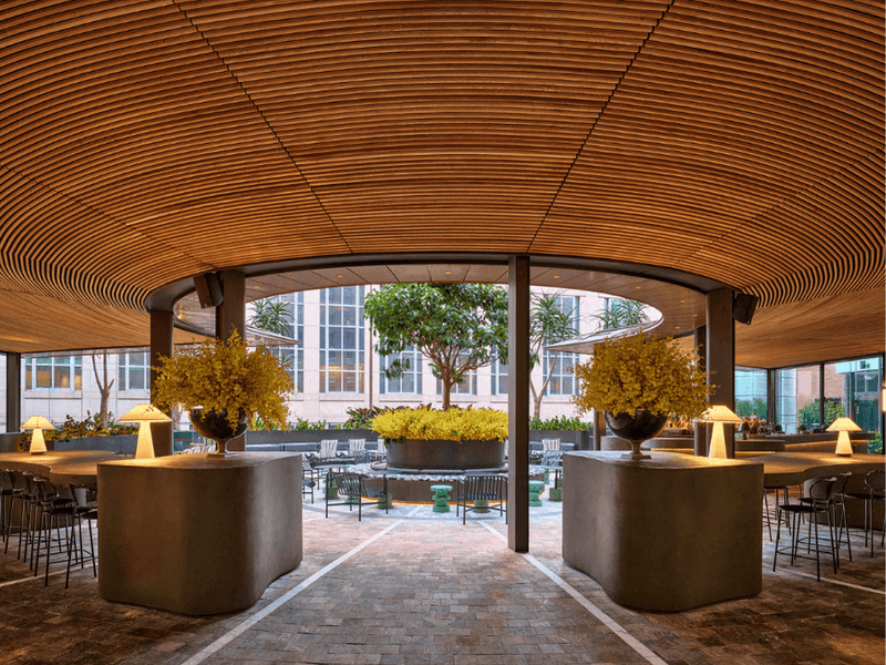 Elegant circular lounge with wooden ceiling, tables, and yellow flower centerpieces under soft lighting.