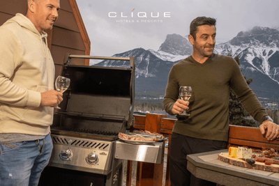 Two men enjoy a meal with wine on a balcony, with a barbecue grill and a stunning view of mountains at Falcon Crest Lodge