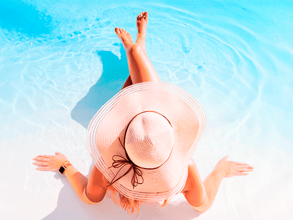Woman relaxing in a pool, wearing a sun hat and floating in blue water with ripples.