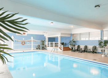 Lounge chairs by an indoor pool under a blue ceiling at Rodd Charlottetown Hotel, an apartment hotel in PEI