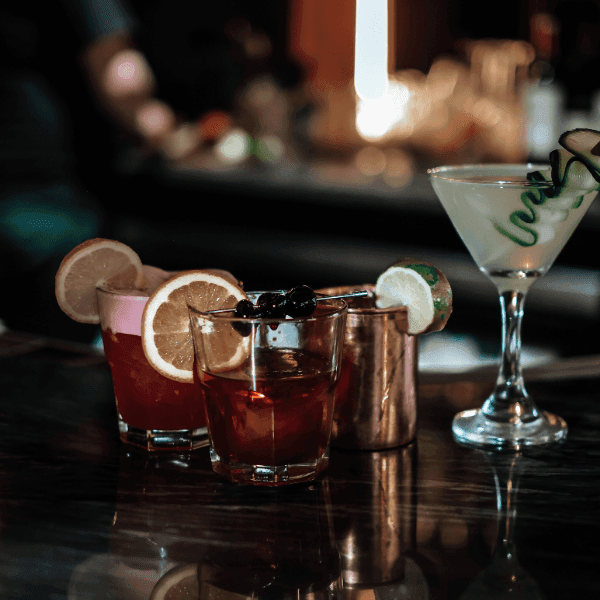 Cocktails garnished with citrus slices, cherries, and cucumber curls on a dark bar counter at La Tourelle Inn and Spa lounge