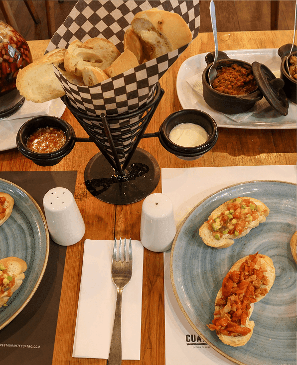 Bruschettas variadas en platos azules con cesta de pan y salsas en Unika Hotels, uno de los mejores hoteles de Bogotá