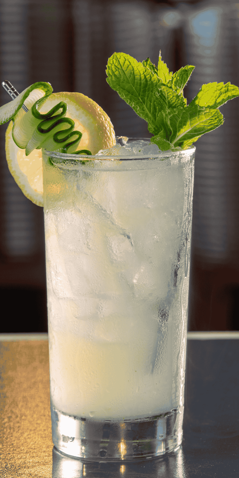 Garnished cocktail with a mint sprig, a lemon wheel, and a cucumber skewer beside frosted glass at La Tourelle Inn & Spa