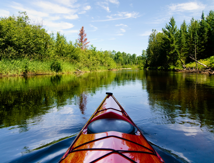 Red kayak on a calm river between dense green trees and grass under a partly cloudy sky near Avon Old Farms Hotel