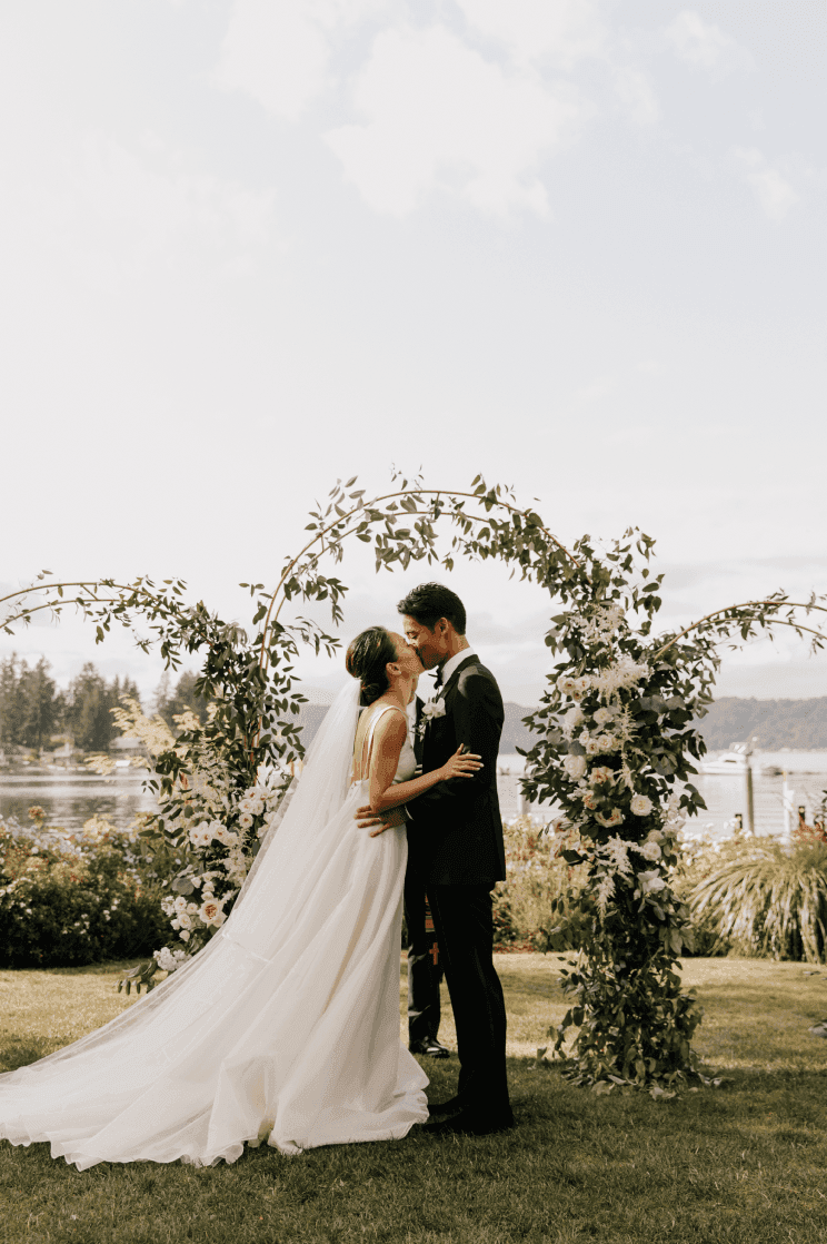 Wedded couple kissing by floral arch at Alderbrook Resort & Spa