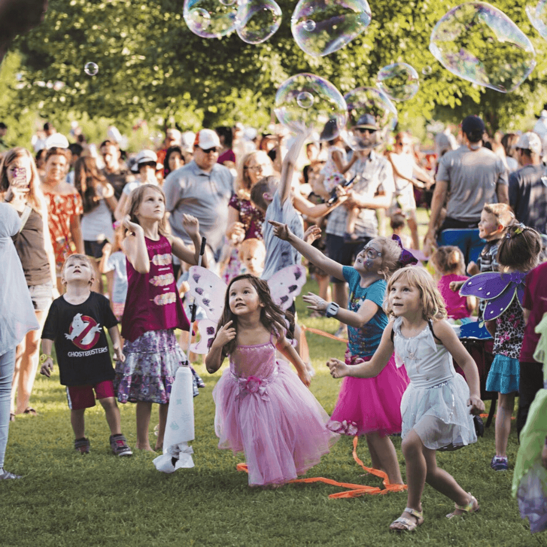 A group of kids in costumes chasing bubbles in the park