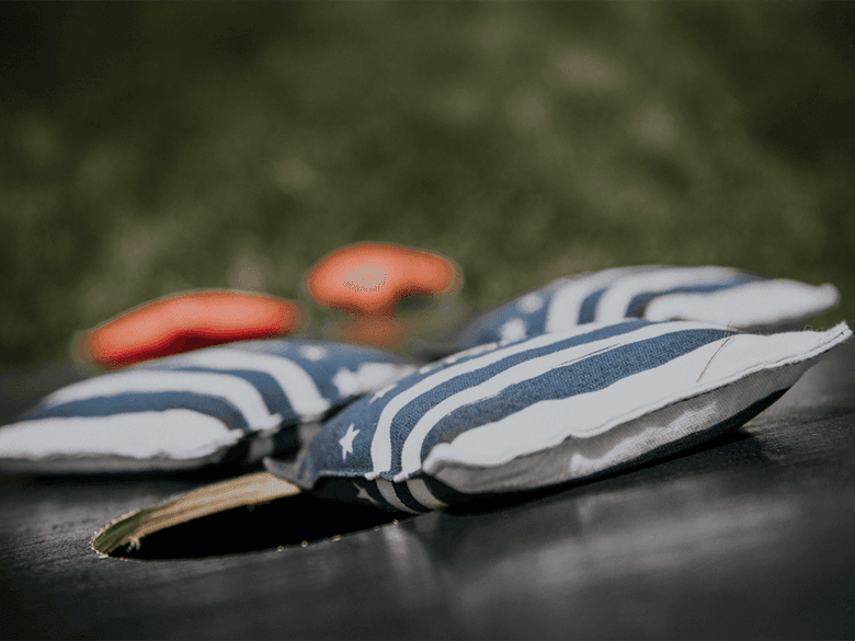 Two bean bag toss game bags lie on a wooden surface with two orange bean bag toss game pieces in the background.