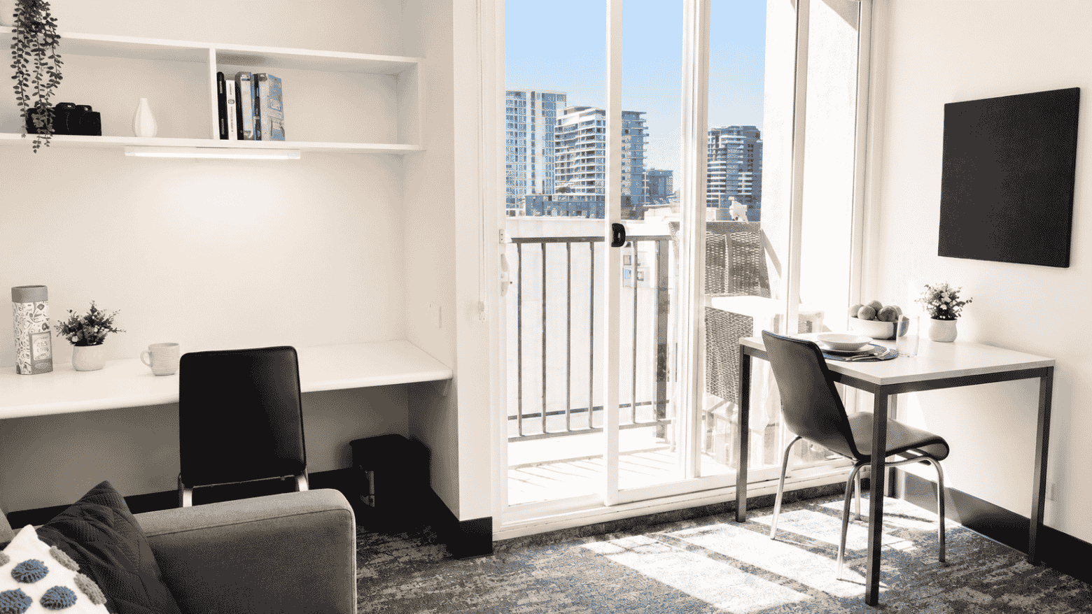Modern student living space with desk, chair, built-in shelving, and balcony overlooking city skyline at Student Living - Waymouth