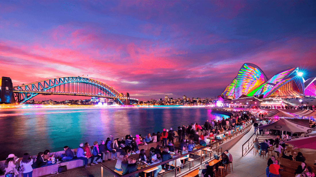 Crowds gather by illuminated Sydney Opera House and Harbour Bridge at dusk during Vivid Sydney 2026.