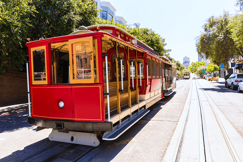 Red and yellow cable car on track beside road and trees at Warwick San Francisco سان فرانسيسكو