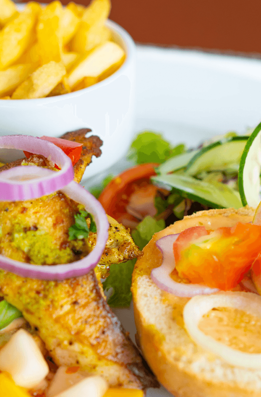 Colorful plate featuring grilled chicken with onions, fresh salad, & a side of golden fries at Bay Gardens Beach Resort & Spa
