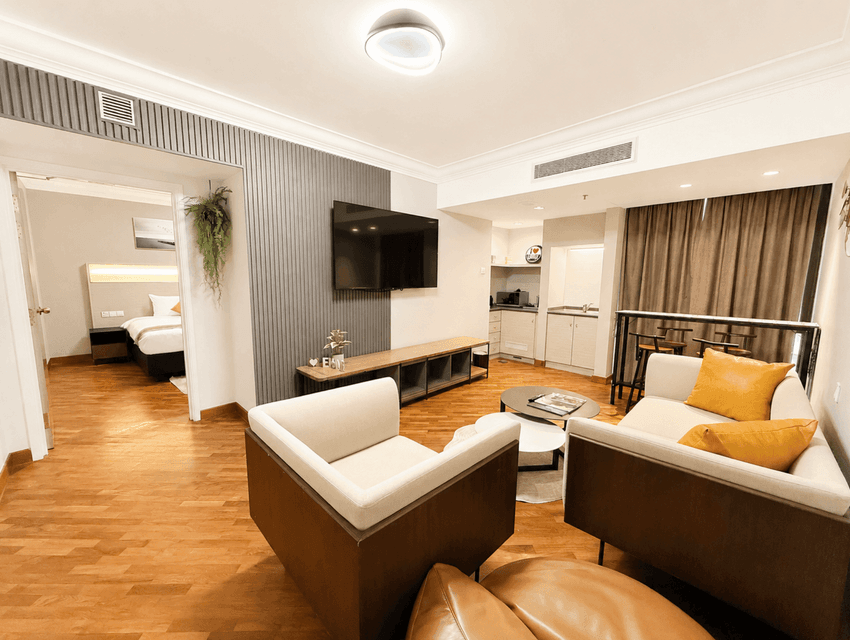 Living room with a wall-mounted TV and an open bedroom doorway in the One Bedroom Serviced Suite at YWCA Fort Canning
