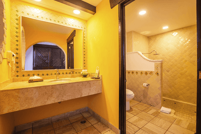 A bathroom with a yellow theme, featuring a sink, mirror, toilet, and shower area.