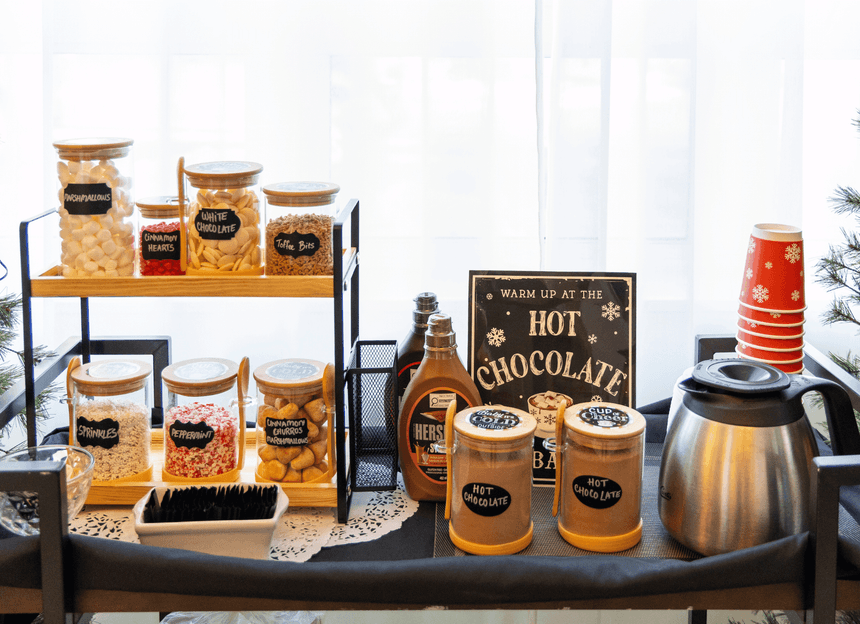 Hot chocolate station with topping jars, syrup bottles, and red cups on a buffet cart display at Rodd Moncton