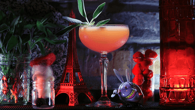 A vibrant cocktail garnished with fresh herbs, colorful decor, and red glass containers at The Gaythering