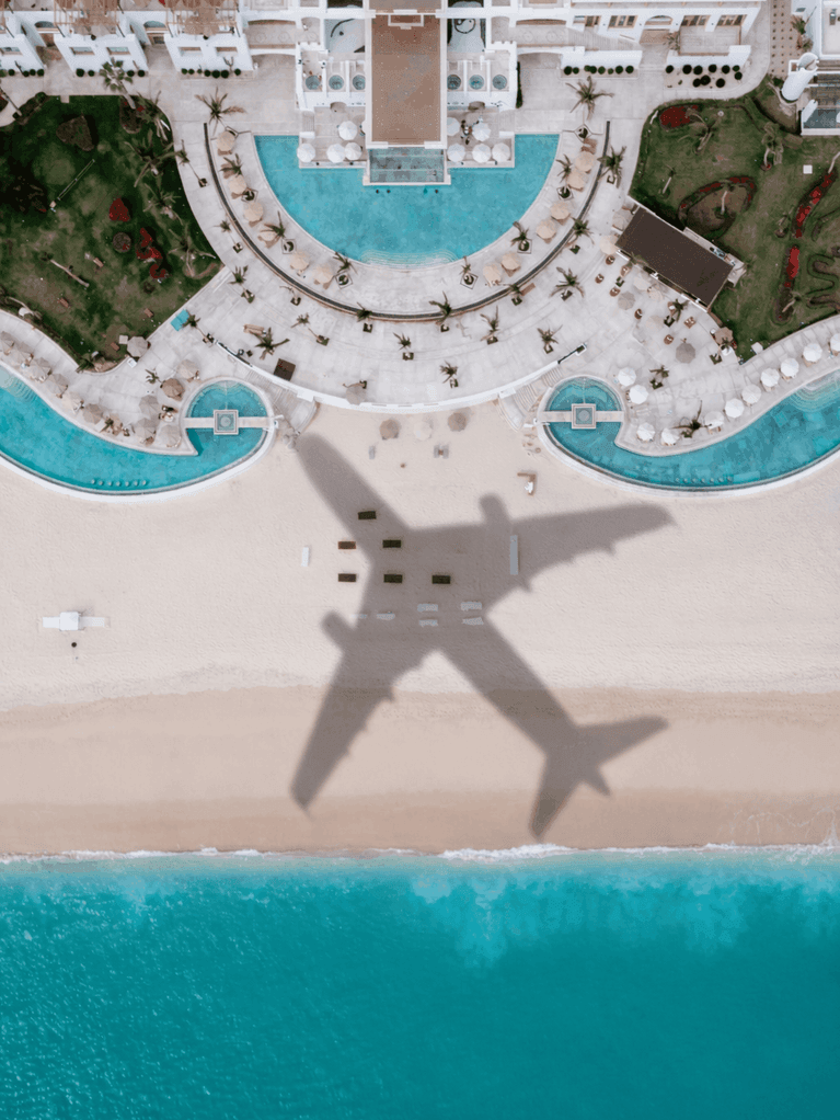 Aerial view of beach resort with pools, loungers, sand, and ocean waters.