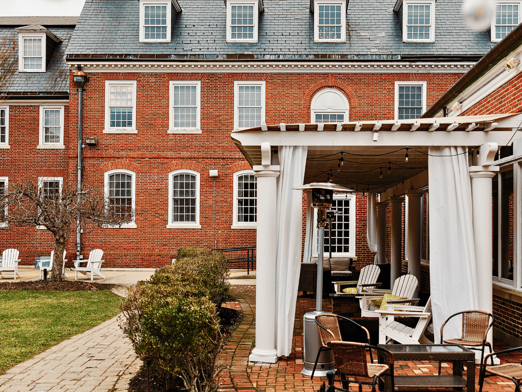 Brick building with outdoor dining area under a pergola with white curtains.