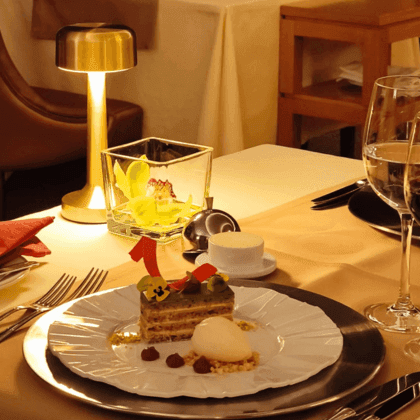 Mesa decorada con plato de postre, cubiertos, copas de vino y lámpara en un ambiente elegante.