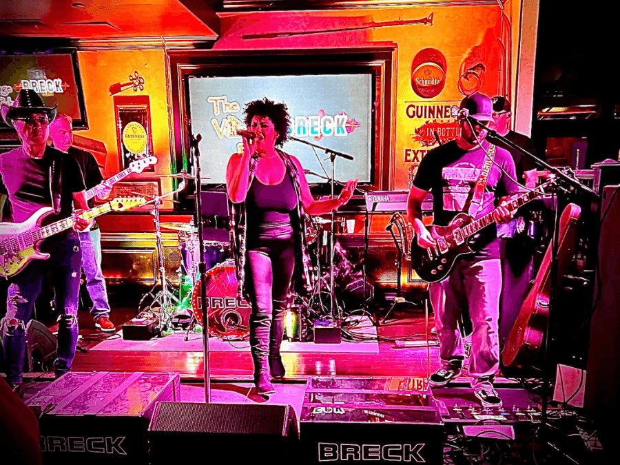 BRECK live band 5 band members on stage 3 male guitarists, a female lead singer, and a drummer with pink & orange lighting.