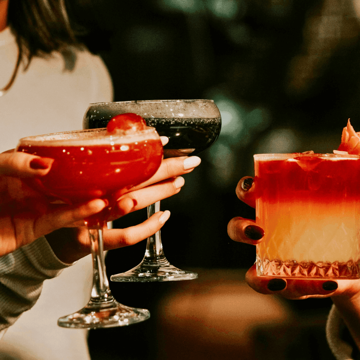 Three people holding cocktail glasses filled with red drinks, garnished with orange peel and cherry at The Exeter Inn