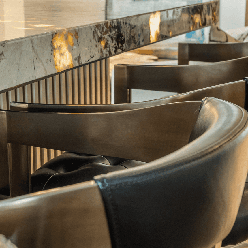 Curved leather barstools placed next to a shimmering, illuminated marble bar counter at The Embers Hotel