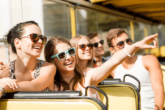 Tourists laugh on an open-top bus by window railings under bright sunshine near Paramount Hotel Seattle