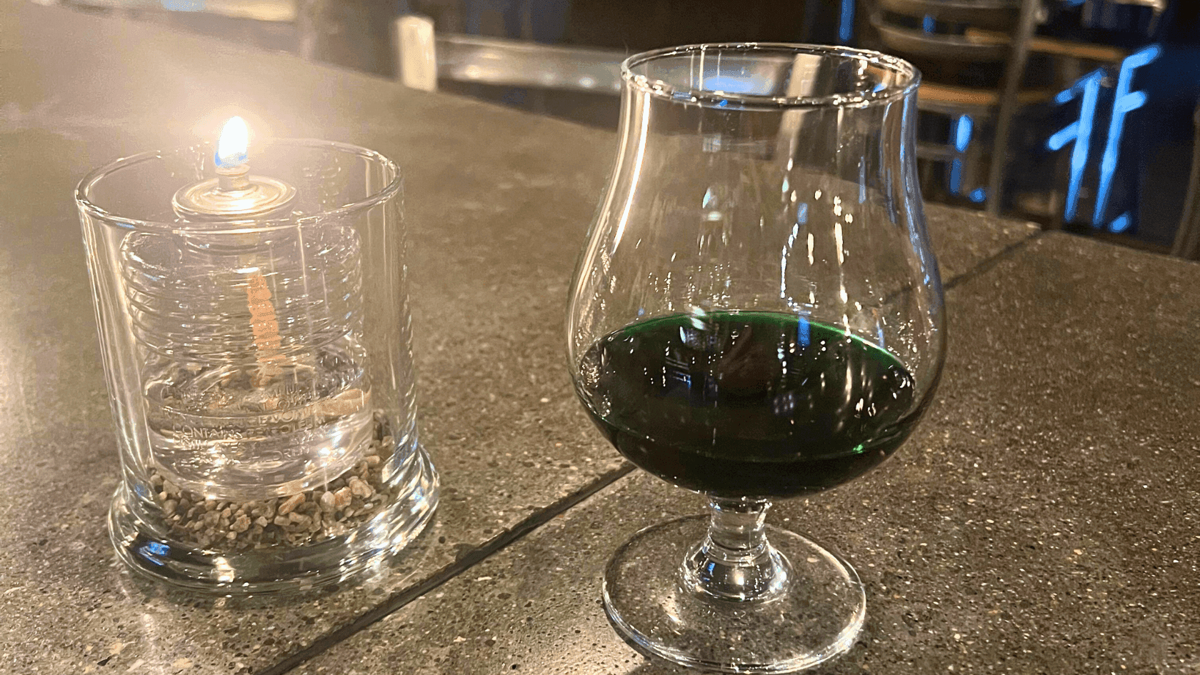 Creme de menth in a glass and a lit candle in a glass on a table.