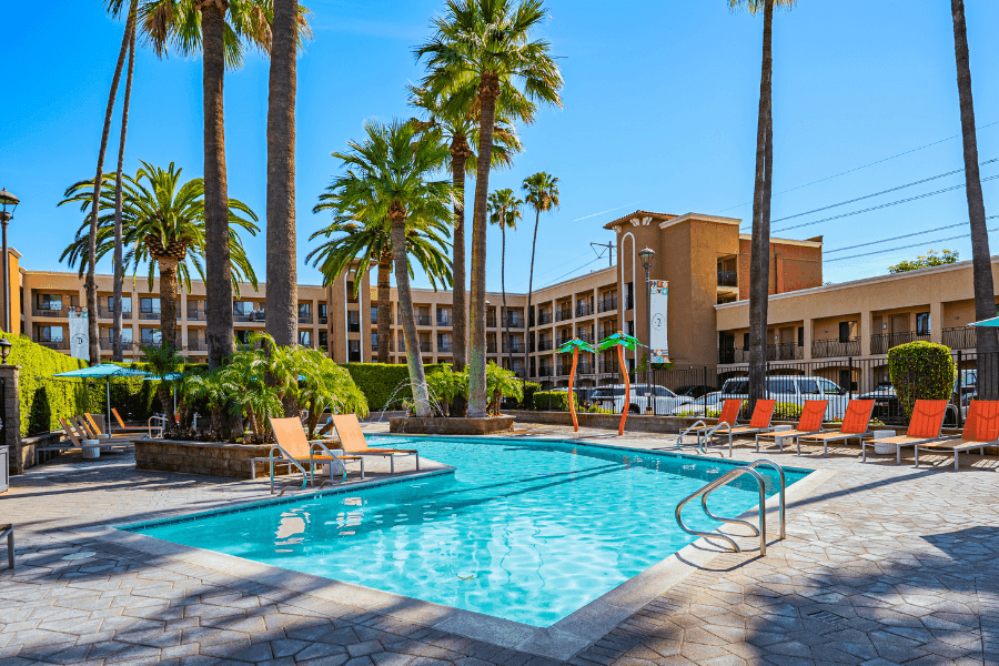 A swimming pool with lounge chairs and palm trees in front of a hotel building.