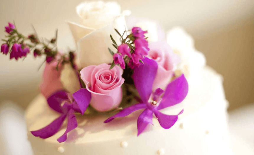 Close-up of a wedding cake with pink roses and purple orchids by pearl beading at The Glenmore Inn & Convention Centre