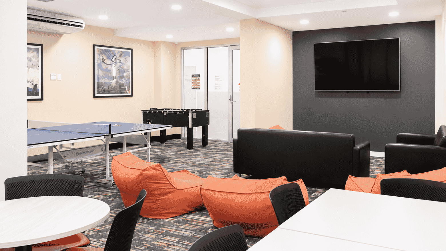 Modern student recreation room with orange bean bags, ping pong table, foosball table, and wall-mounted TV at Student Living - Waymouth