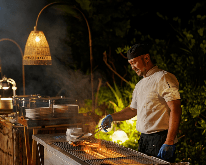 A chef grilling food at night in an outdoor setting for BBQ at Grand Park Kodhipparu