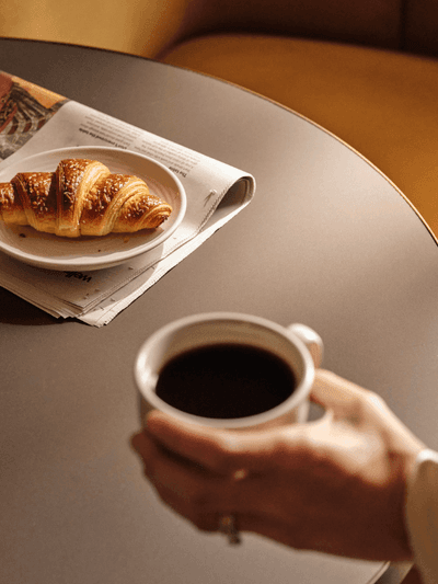 Woman in a dress stands on a balcony overlooking a building from a hotel room.