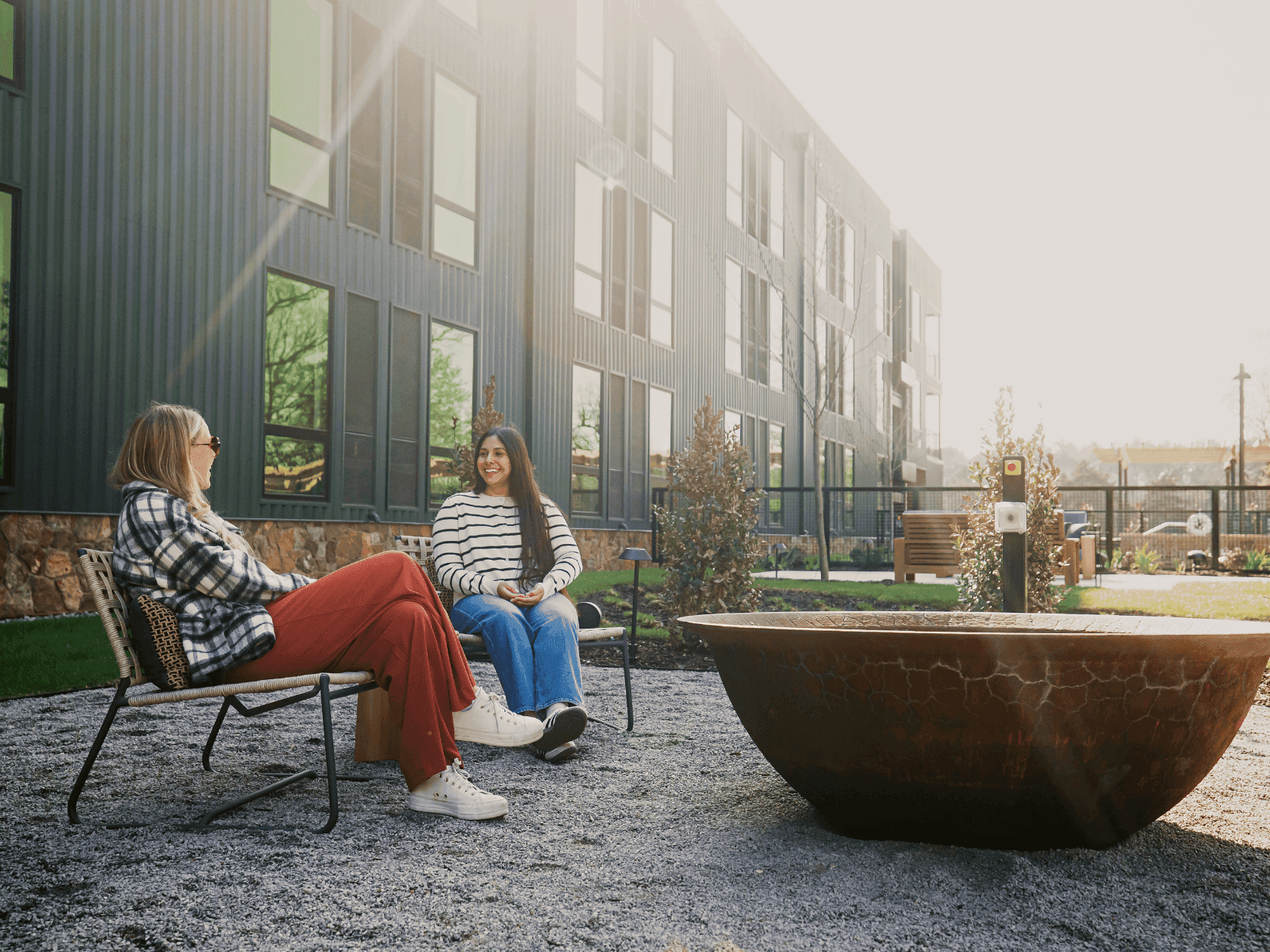 Two women sitting on chairs with a modern building in the background, promoting Advance Purchase Rate.