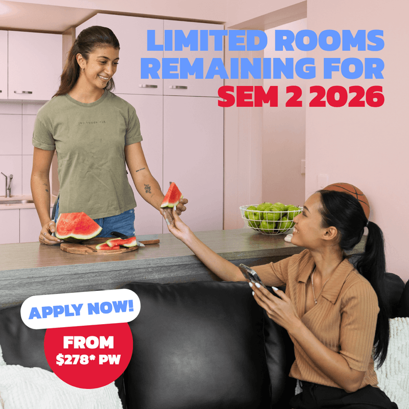 Two students sharing watermelon in a modern kitchen with white cabinets and a fruit bowl at UniLodge Darwin