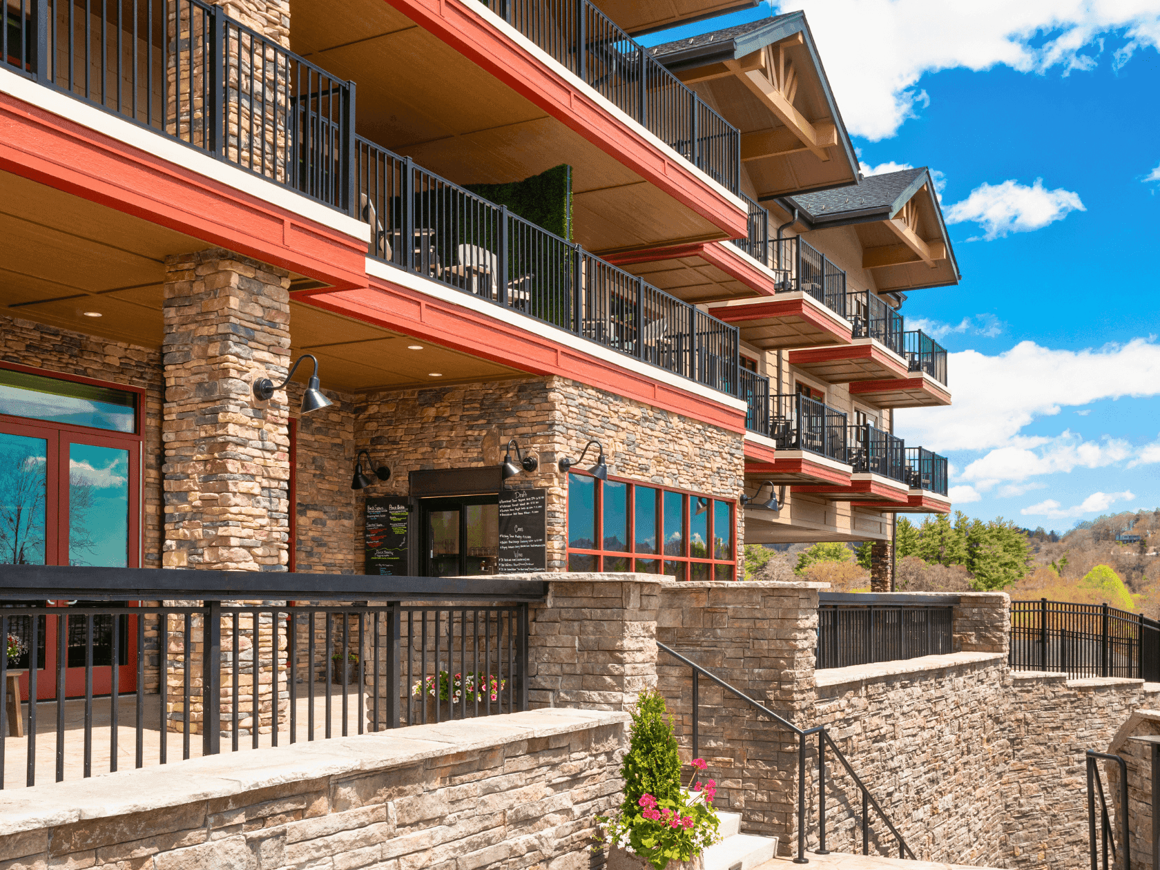 Stone building exterior with balconies, black railings, red accents, and a blue sky in the background.