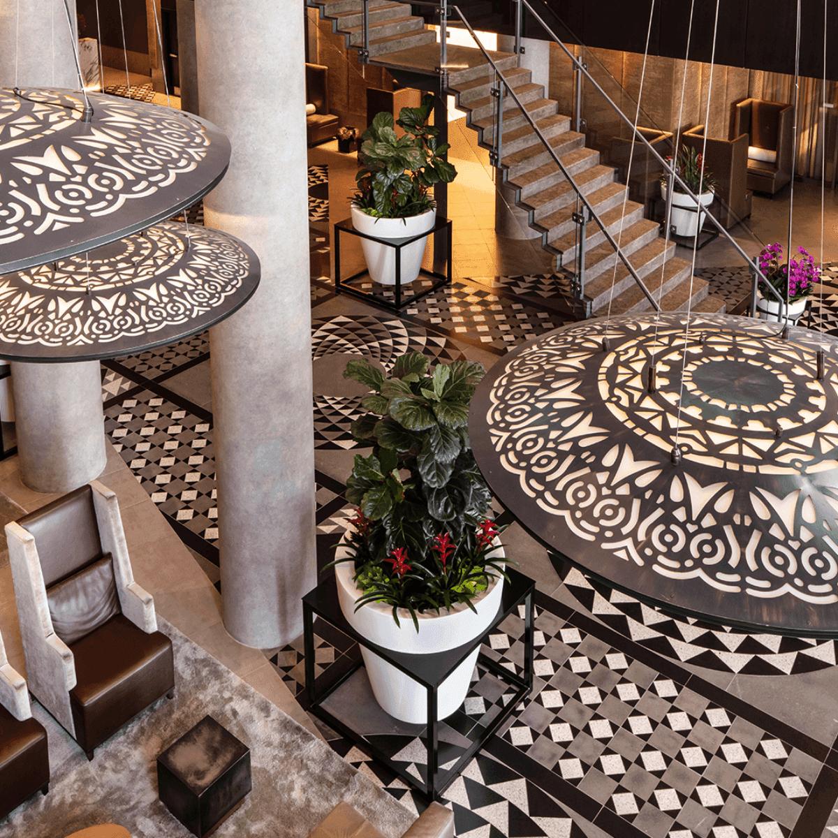 Patterned pendant lamps hang over potted plants by a staircase, on geometric tiled floors at the Hotel X Toronto