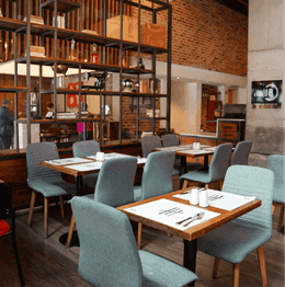 Restaurant with wooden tables and blue chairs by open shelving and brick walls at Unika Hotels, an elite Bogota hotel