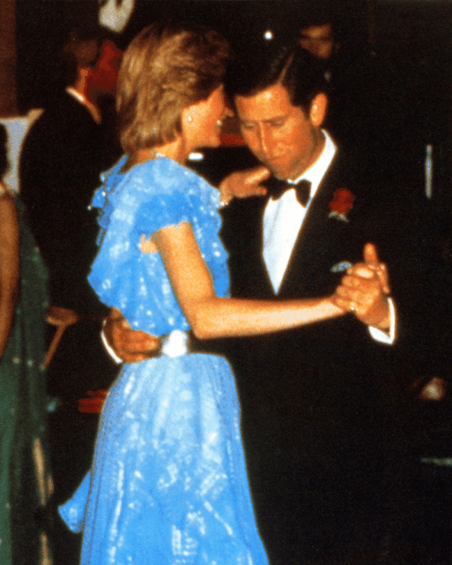 A man and woman, dressed formally, are dancing together in a social setting with others nearby.