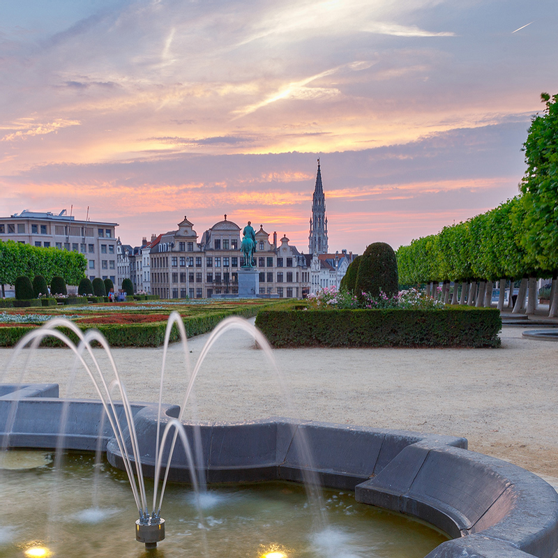 A scenic park near Warwick Hotels and Resorts featuring a fountain, manicured hedges, and historic buildings in Brussels