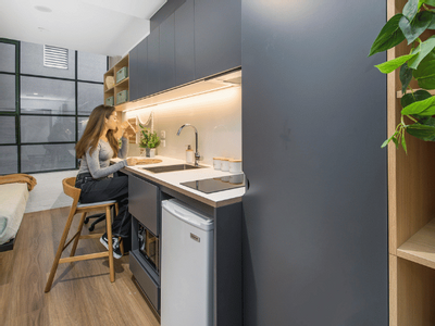 Woman seated at small kitchen counter in a studio apartment with modern design.