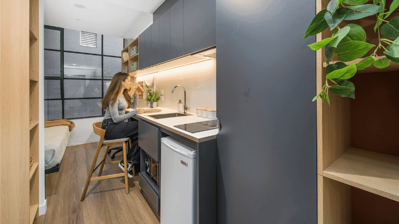 Woman seated at small kitchen counter in a studio apartment with modern design.