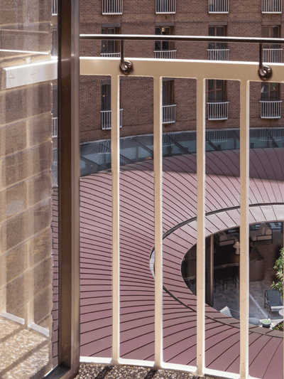 Hotel balcony with wooden railing overlooking circular courtyard garden with palm trees and landscaping