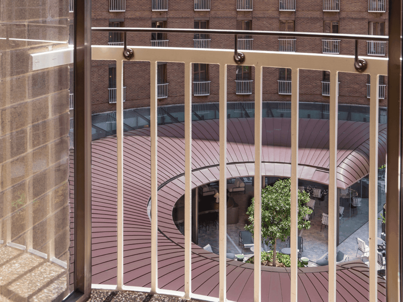Hotel balcony with wooden railing overlooking circular courtyard garden with palm trees and landscaping