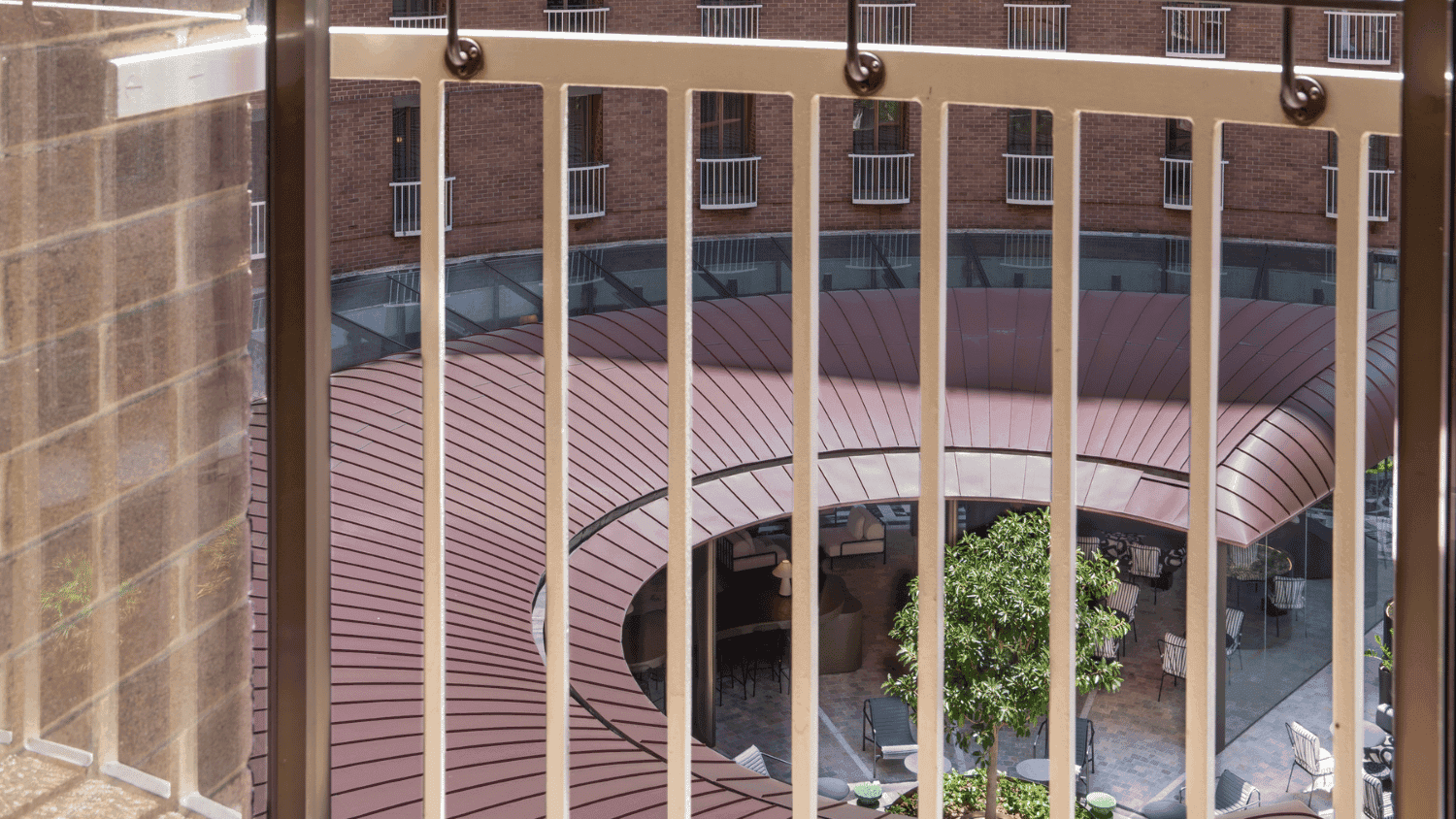 Hotel balcony with wooden railing overlooking circular courtyard garden with palm trees and landscaping
